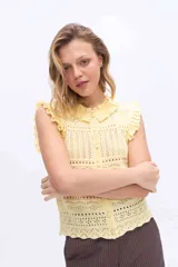 Chaleco tejido de punto color amarillo, con diseño calado, escote redondo y volados en los hombros y cuello. Cuenta con cierre frontal de botones forrados al tono.