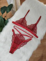 Conjunto de lencería de encaje rojo, compuesto por un bralette triangular con tirantes finos y una tanga con diseño de tiras cruzadas y detalles artesanales.