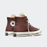 Championes Converse modelo Chuck 70, de caña alta, confeccionados en lona color marrón con suela de goma blanca y puntera reforzada. Presentan el icónico parche circular con el logo de la marca en el lateral interno, cordones blancos y costuras reforzadas.