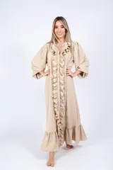 Vestido largo color crudo, estilo camisero, con cuello en V y volados verticales en el frente. Tiene mangas largas abullonadas y corte amplio.