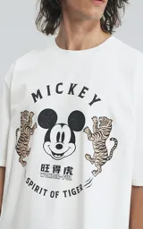 Remera de manga corta con cuello redondo y calce oversize, confeccionada en algodón premium. Presenta un estampado frontal con la cara de Mickey Mouse rodeada de dos tigres y texto alusivo.