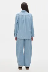 Camisa oversized de jean color crema, con botones rojos en forma de fresa y pespuntes a contratono. Tiene el logo "PASTICHE" bordado en rojo en el pecho.