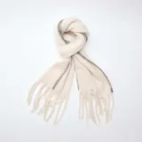Bufanda de tejido suave color beige, con flecos en los extremos y detalle de costura decorativa en zigzag a lo largo de los bordes.