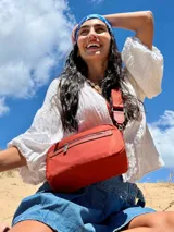 Bandolera de diseño moderno y funcional, confeccionada en nylon color marrón claro. Cuenta con múltiples compartimentos con cierre metálico, herrajes plateados y una correa ancha ajustable con detalle de marca.