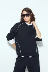 Canguro negro de silueta amplia con capucha integrada y detalles de líneas blancas que recorren el frente y las mangas.