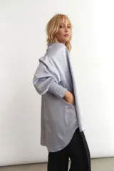 Camisa celeste de seda sintética, corte holgado, mangas largas abullonadas con puños elásticos y bolsillos laterales.