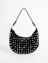 Cartera tipo bandolera de gamuza negra en forma de media luna, completamente decorada con tachas metálicas plateadas de distintos tamaños. Cuenta con un asa ajustable para llevar al hombro o en la mano y cierre superior con cremallera.