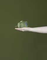 Charm en forma de mini bolso color verde militar, con asas pequeñas, etiqueta con logo y gancho de metal tipo mosquetón.