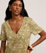 Vestido corto tipo t-shirt color verde oliva con estampado de paisaje tropical en tonos beige. Tiene escote en V y mangas cortas.