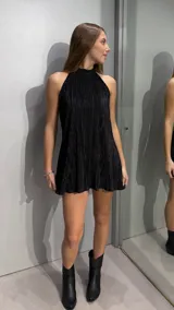 Vestido corto de color negro con textura plisada, diseño sin mangas y cuello alto tipo halter.