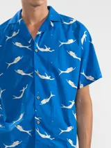 Camisa celeste con estampado de sirenas blancas, de corte recto con cuello camisero y mangas cortas.