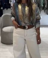 Sweater de tejido de punto con diseño abstracto en tonos beige, camel, azul y detalles en dorado brillante. Presenta cuello redondo, mangas largas con puños acanalados y un corte holgado.