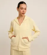 Campera deportiva color amarillo pastel, con capucha ajustable con cordón, cierre frontal con cremallera, bolsillos laterales y puños elásticos.