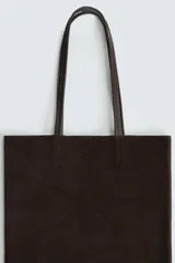 Bolso tipo shopper de diseño minimalista, confeccionado en piel con acabado de serraje. Cuenta con dos asas largas de mano y un compartimento principal espacioso con un bolsillo interior con cierre.
