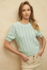 Top de tejido tramado color verde menta, de manga corta y cuello redondo. Presenta un patrón calado ondulado y elástico en el ruedo y los puños de las mangas.