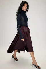 Falda midi asimétrica de color bordó, confeccionada en tejido satinado con volumen. Presenta un diseño con volados en la cintura y cierre de cremallera oculta en la espalda.