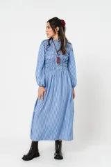 Vestido largo a rayas verticales azules y blancas, con manga globo y diseño de nido de abeja con hilo elástico hasta la cintura. Cuello alto fruncido y falda amplia con caída fluida.