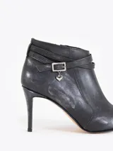 Bota corta de cuero vacuno color negro con acabado metalizado, taco fino mediano y punta fina. Presenta una tira decorativa con hebilla metálica y un dije en forma de corazón. Cuenta con cierre lateral para un calce cómodo y está completamente forrada en cuero.