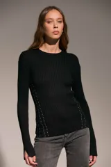 Sweater de punto acanalado en color negro, con cuello redondo y mangas largas. Presenta detalles de tachas metálicas plateadas dispuestas en líneas verticales a los costados del torso.