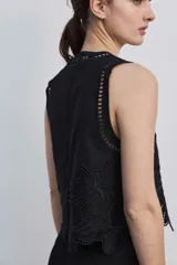 Blusa sin mangas de corte crop en color blanco, con detalles de bordados calados en tono tostado formando diseños florales en el cuello, los hombros y el borde inferior.