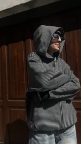 Campera con capucha y cierre frontal, de tejido grueso color gris oscuro con rayas horizontales finas en blanco. Presenta cuello alto y puños y cintura acanalados.