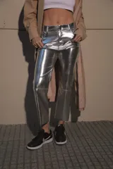 Pantalón de ecocuero metalizado color plateado, de corte capri semi oxford y tiro medio-alto. Presenta cierre frontal con botón metálico y costura horizontal a la altura de la rodilla.
