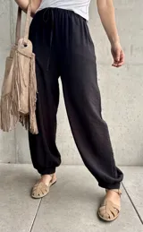 Pantalón negro tipo babucha con cintura elástica fruncida y cordón ajustable, corte holgado y puños elásticos en los tobillos.