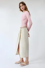 Falda midi de tiro medio color beige, con pliegues en la parte delantera, abertura frontal en el bajo y cinturón combinado a tono con hebilla metálica.