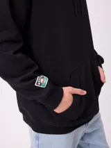 Canguro negro con capucha y estampado grande en la espalda de un paisaje con árboles, una camioneta camper y un lago al atardecer, con el logo "RUSTY" en la parte superior.