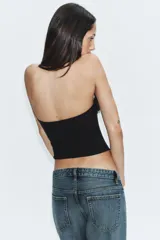 Top corsetero negro de escote recto y hombros descubiertos, con varillas interiores y detalle de aplicaciones de flores de tela en el borde superior. Cuenta con cierre lateral con cremallera oculta.
