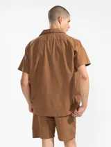 Bermuda de hombre color azul petróleo, confeccionada en mezcla de lino y algodón. Presenta cintura elástica con cordón, bolsillos laterales y trasero tipo parche. Incluye bordado floral en la pierna izquierda y etiqueta con logo en el bolsillo trasero.