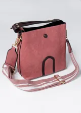 Cartera tipo bucket color rosa con detalles en marrón. Tiene correa de hombro ajustable con rayas horizontales blancas y rosas.