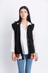 Chaleco negro de lana merino tejido a crochet, con botones de madera y apliques de flores de colores en el ruedo.