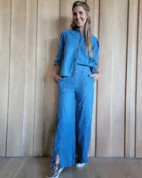 Pantalón de denim de corte amplio y tiro medio, con bolsillos frontales tipo parche, costuras verticales decorativas y tajos laterales en el ruedo. Cuenta con pretina frontal fija y elástico en la parte posterior.