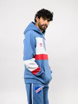 Canguro con capucha de Umbro del Club Nacional de Football, con diseño de bloques de color en azul, blanco y rojo. Presenta bolsillo frontal tipo canguro, cordones ajustables en la capucha y logos bordados del club y la marca.