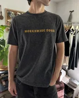Remera blanca de manga corta, corte regular y cuello redondo, con gran estampado en la espalda de temática "Worldwide Tour" con una calavera y texto en rojo, azul y blanco.