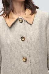 Tapado largo de lana fina con diseño de espiga en tonos beige. Presenta cuello camisero y solapas de bolsillos en cuero color suela, con cierre frontal de botones a tono.