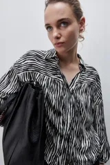 Camisa de calce amplio confeccionada en viscosa fluida con estampado animal print tipo cebra en blanco y negro. Presenta cuello camisero, escote en V y mangas largas con puños elastizados, además de frunces en el canesú que aportan volumen.