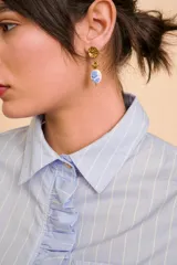 Aros colgantes dorados con base texturizada y dije de cerámica blanca con diseño floral en azul.