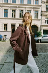 Chaqueta marrón de efecto ante con cuello solapa, manga larga, bolsillos delanteros de plastrón, cierre frontal con botones y cinturón a juego.