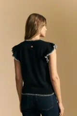 Top tejido sin mangas color negro, con cuello redondo y volados en las sisas con terminación en contraste de punto blanco. Presenta un calce recto y puño inferior acanalado con detalle de punto blanco.