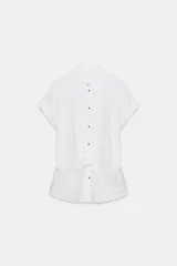 Camisa blanca confeccionada en tejido con lino, con cuello solapa y manga muy corta con terminación en vuelta. Presenta un detalle de nudo en el delantero y cierre frontal con botones metálicos.