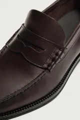Mocasín de vestir para hombre fabricado en piel de color marrón oscuro, con detalle de antifaz en el empeine y suela con ligero tacón.