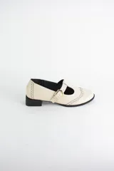 Zapato tipo guillermina estilo oxford, confeccionado en cuero negro con detalles de perforaciones decorativas en la puntera y cierre mediante tira con hebilla metálica dorada. Presenta un taco bajo cuadrado.