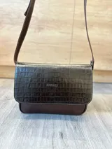 Cartera bandolera de cuero vacuno color bordó, con solapa frontal de textura símil cocodrilo y detalles de costuras pespunteadas en blanco. Cuenta con correa ajustable y cierre superior.