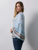 Blusa celeste de gasa bordada, con escote en V y lazo de ajuste. Mangas largas con terminación amplia.