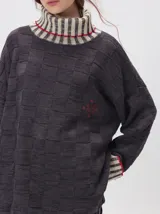 Pullover de punto jacquard con diseño de cuadros en relieve, cuello alto y mangas largas. Presenta detalles de pespuntes en color rojo en el cuello y los puños, aberturas laterales y logo bordado en el pecho.