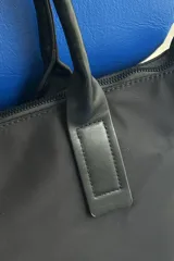 Cartera tipo shopper color negro, de diseño estructurado con doble asa de mano y cierre superior. Presenta sutil grabado de la marca en la parte inferior frontal.