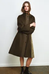 Parka oversize de corte recto confeccionada en tejido con mezcla de lana en color verde oliva. Presenta cuello alto con capucha, cierre frontal con botones y bolsillos laterales. Incluye detalles en tejido acolchado a contraste en la solapa frontal y puños.