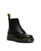 Botas de caña media Dr. Martens modelo 1460, confeccionadas en cuero liso negro. Presentan cierre de cordones con ocho ojales, costuras amarillas distintivas en la suela, suela de goma acanalada con amortiguación de aire y tirador trasero con logo.